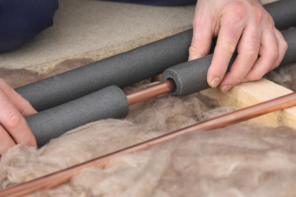 Plumber installing foam insulation on exposed basement pipes